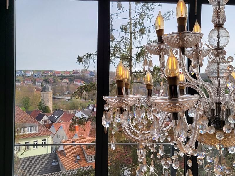 Ein Kronleuchter hängt vor einem Fenster mit Blick auf eine Stadt.