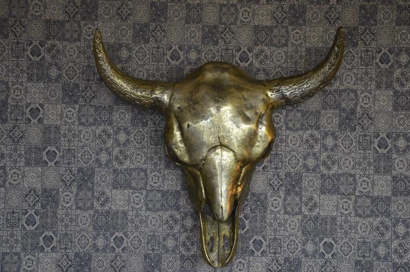 An einer Wand mit gemusterter Tapete hängt ein Stierschädel.