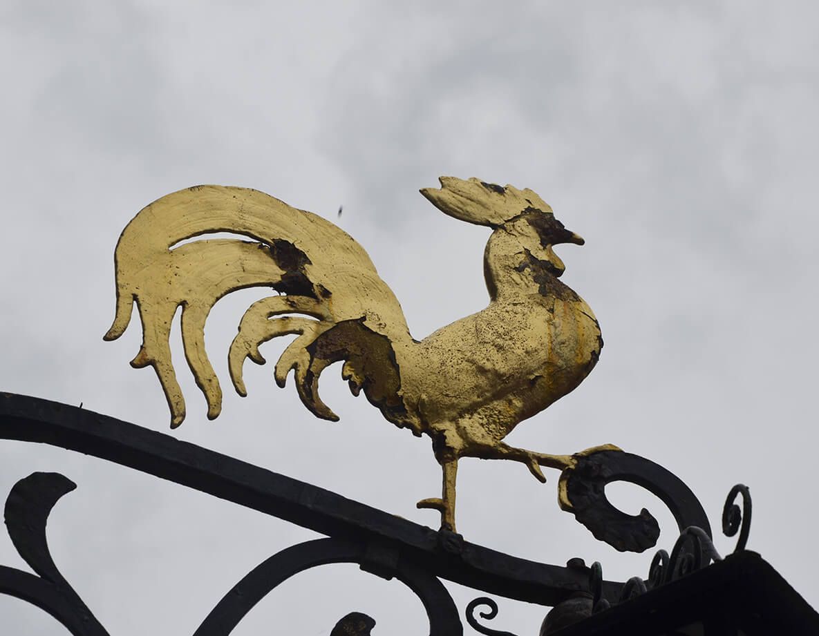 Ein goldener Hahn sitzt auf einem schmiedeeisernen Geländer