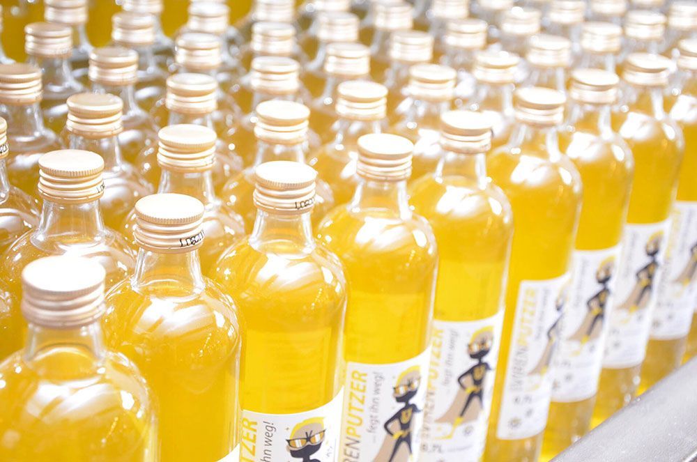 Auf einem Förderband sind mehrere Flaschen mit einer gelben Flüssigkeit aufgereiht.