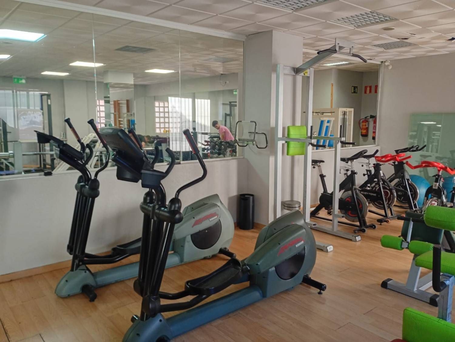 Un gimnasio con dos máquinas elípticas en primer plano y varias bicicletas estáticas al fondo.