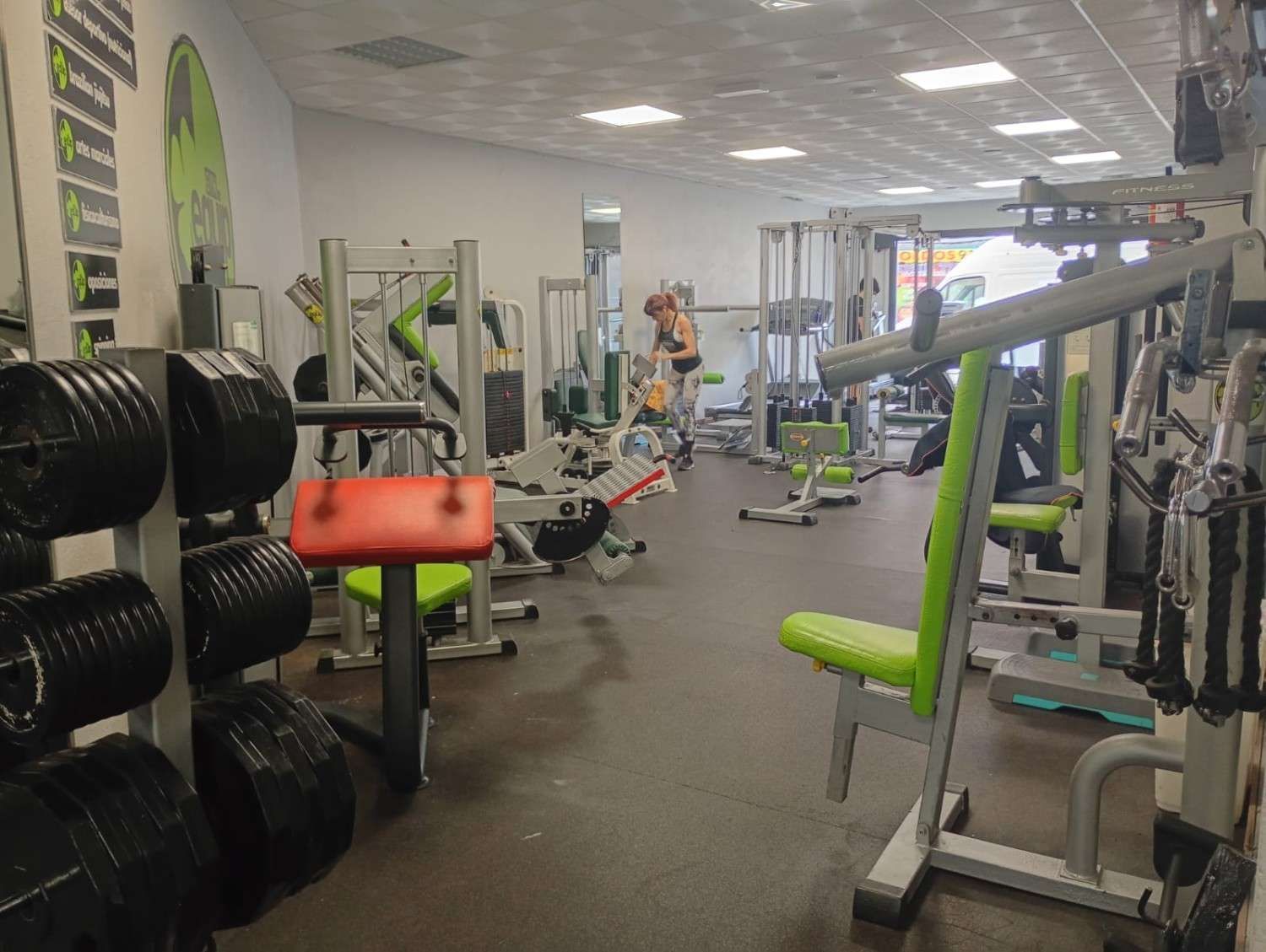 Un grupo de personas en un gimnasio posan para una foto; algunas sonríen y flexionan los brazos, vestidas con ropa deportiva.