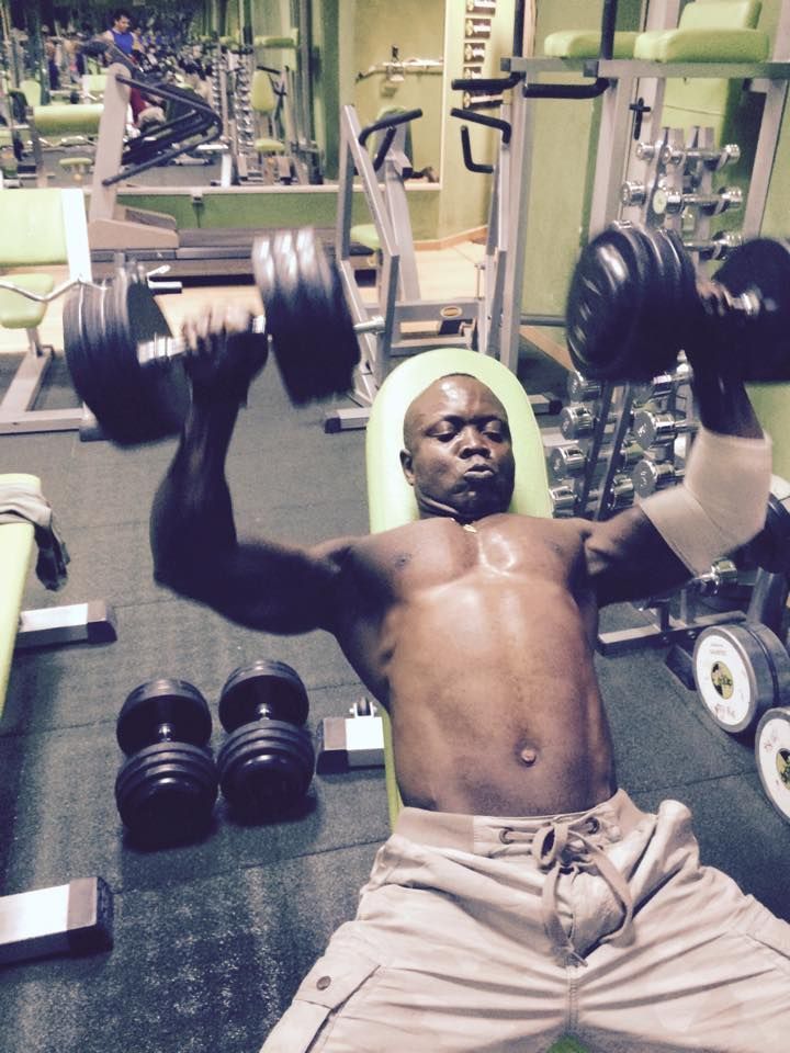 Una persona realiza un press de banca con mancuernas mientras está tumbada en un banco de pesas en un gimnasio.