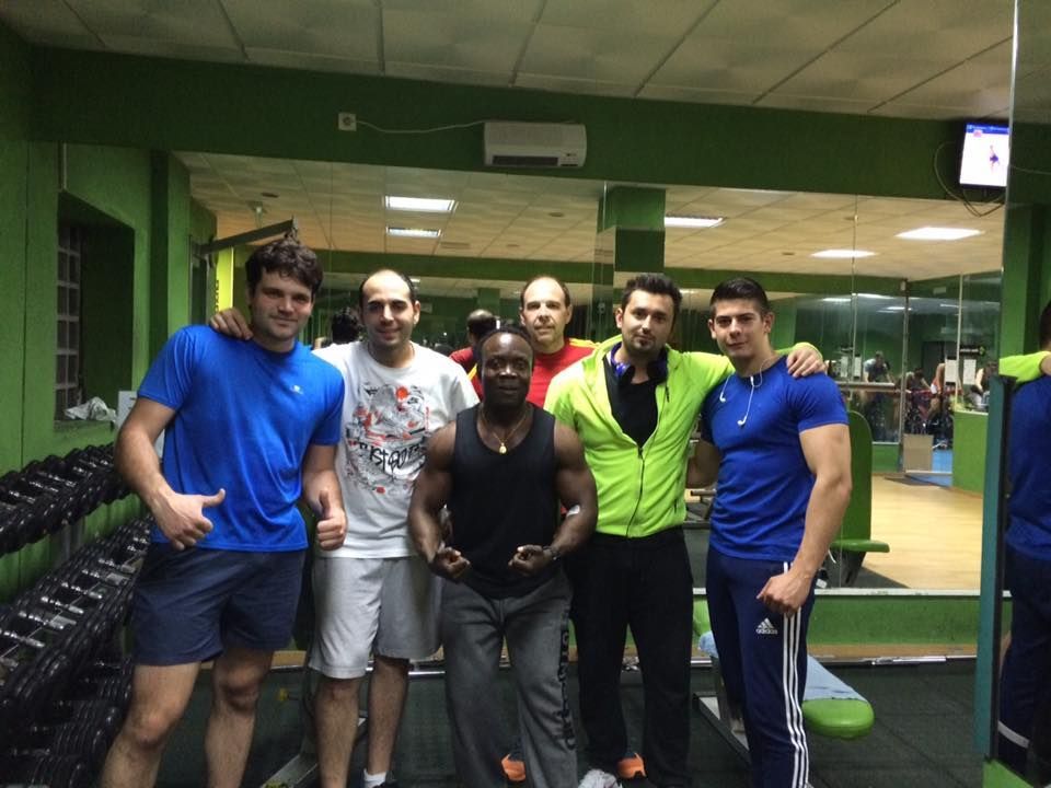 Seis personas posan para una foto de grupo dentro de un gimnasio con paredes verdes y estantes llenos de mancuernas.