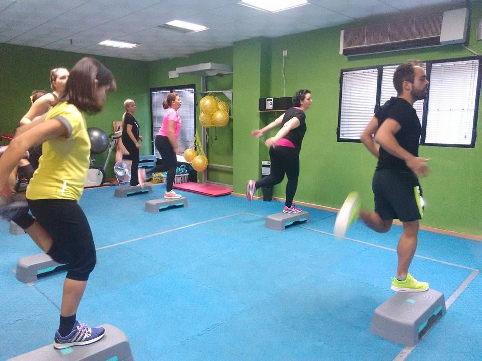 Una clase de fitness en la que se practica aeróbic con step sobre plataformas azules en un gimnasio con paredes verdes.