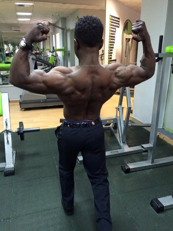 Un culturista posa de espaldas en un gimnasio, mostrando el desarrollo 