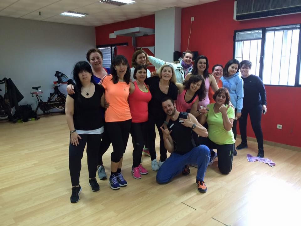 Un grupo de personas posando para una foto en un gimnasio con paredes rojas y suelo de madera.