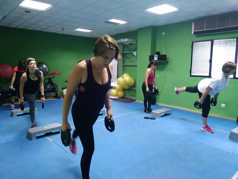 Personas en un gimnasio realizando ejercicios de peso muerto a una sola pierna con pesas de mano sobre un suelo azul.