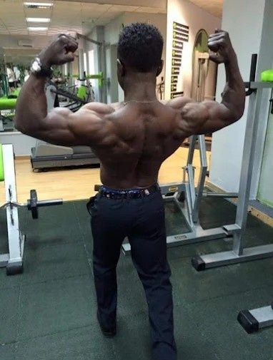 Una persona posando de espaldas en un gimnasio para lucir sus músculos de la espalda y los brazos.