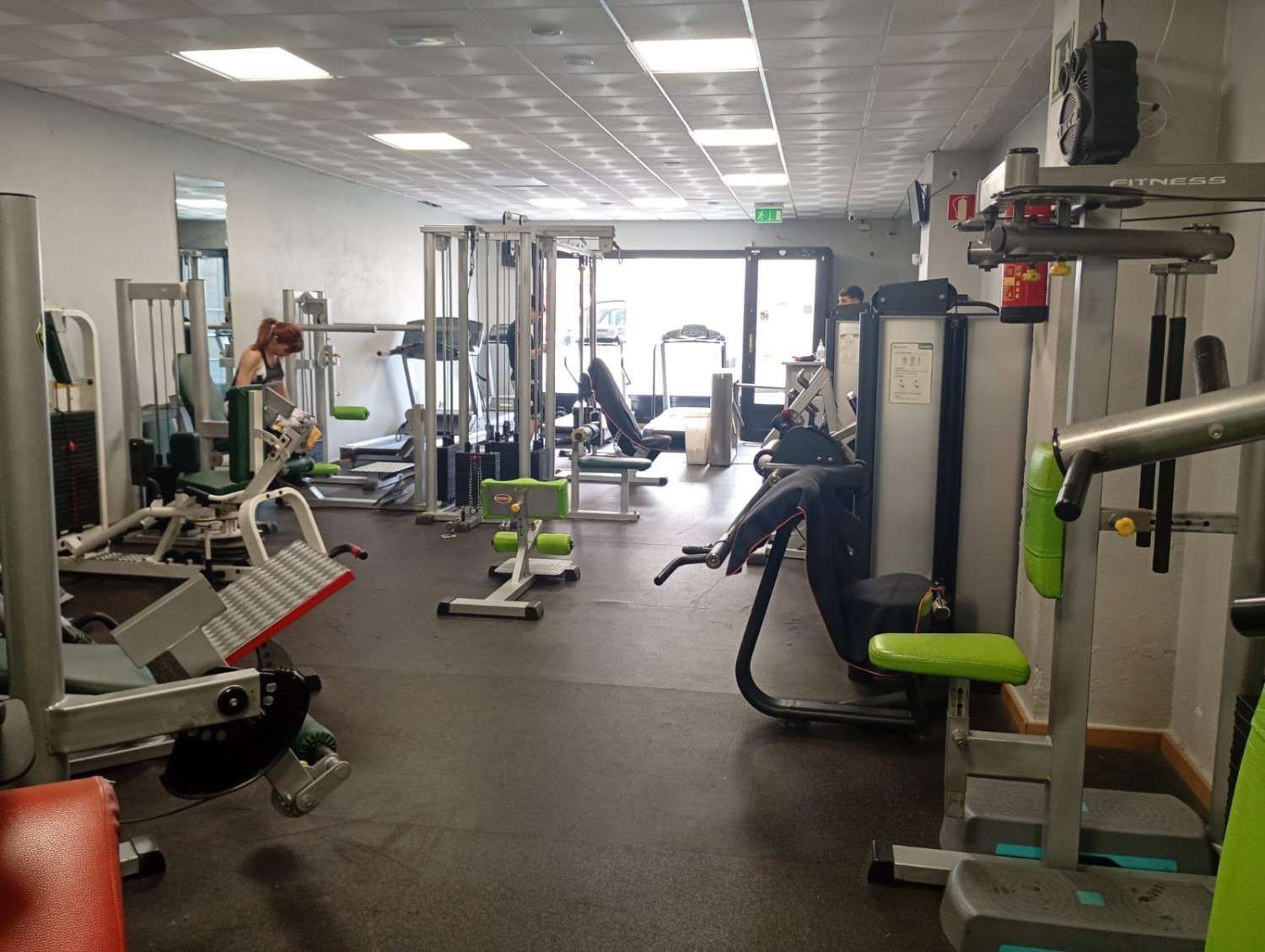 Un gimnasio cubierto con varias estaciones de entrenamiento y aparatos de ejercicio dispuestos sobre un suelo oscuro.