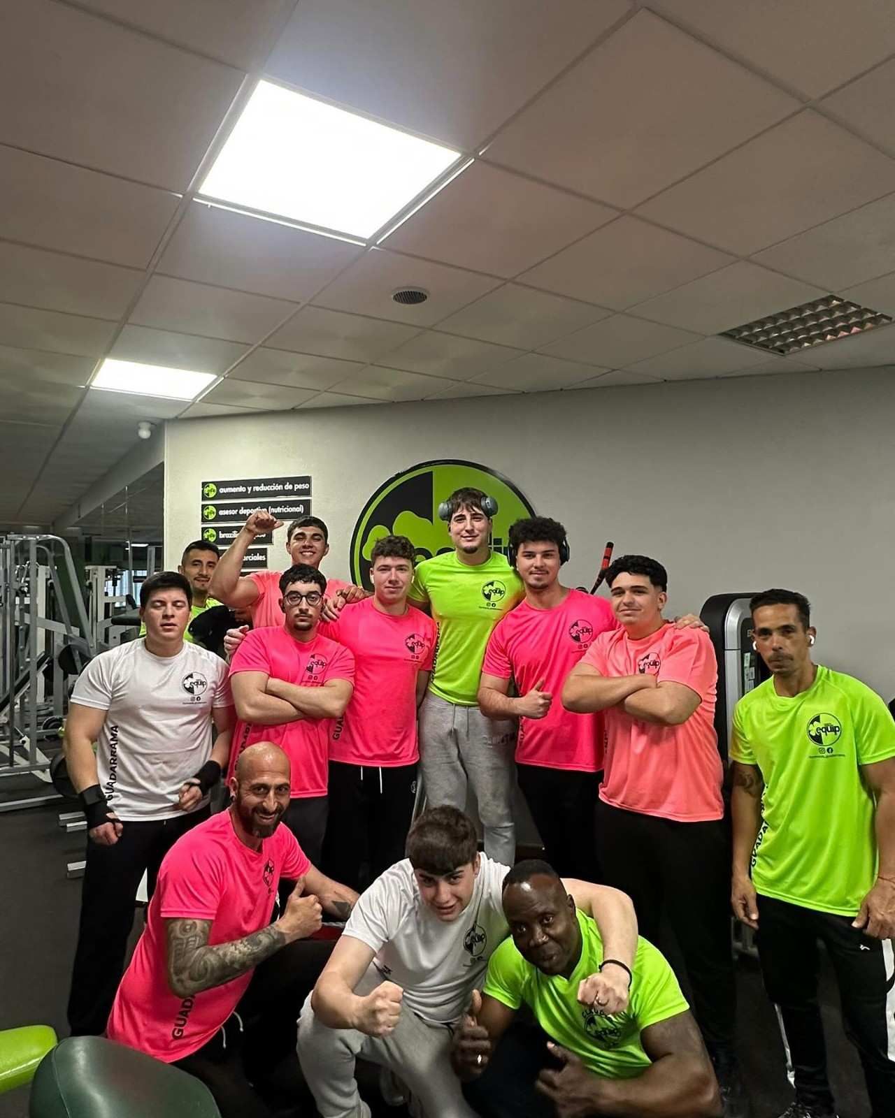 Un grupo de personas con camisetas deportivas de colores llamativos posan para una foto dentro de un gimnasio.