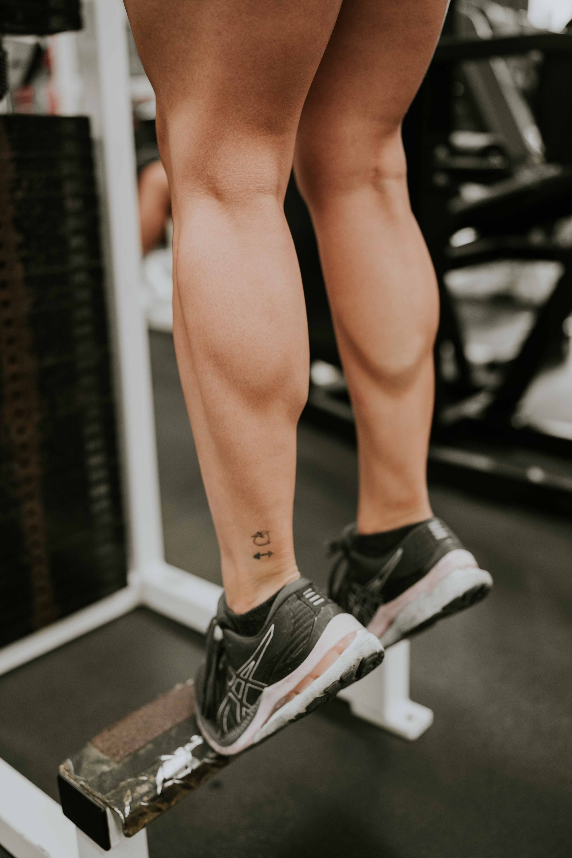 Persona realizando elevaciones de pantorrillas en una máquina de gimnasio, con zapatillas negras y calcetines blancos.