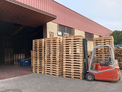 Una carretilla elevadora roja está estacionada frente a un almacén lleno de paletas de madera.