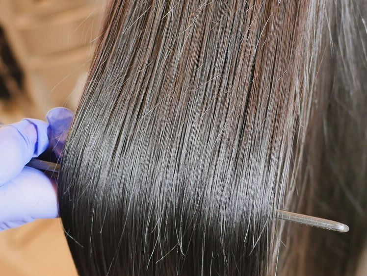 Una persona sostiene un par de tijeras sobre el cabello de una mujer.
