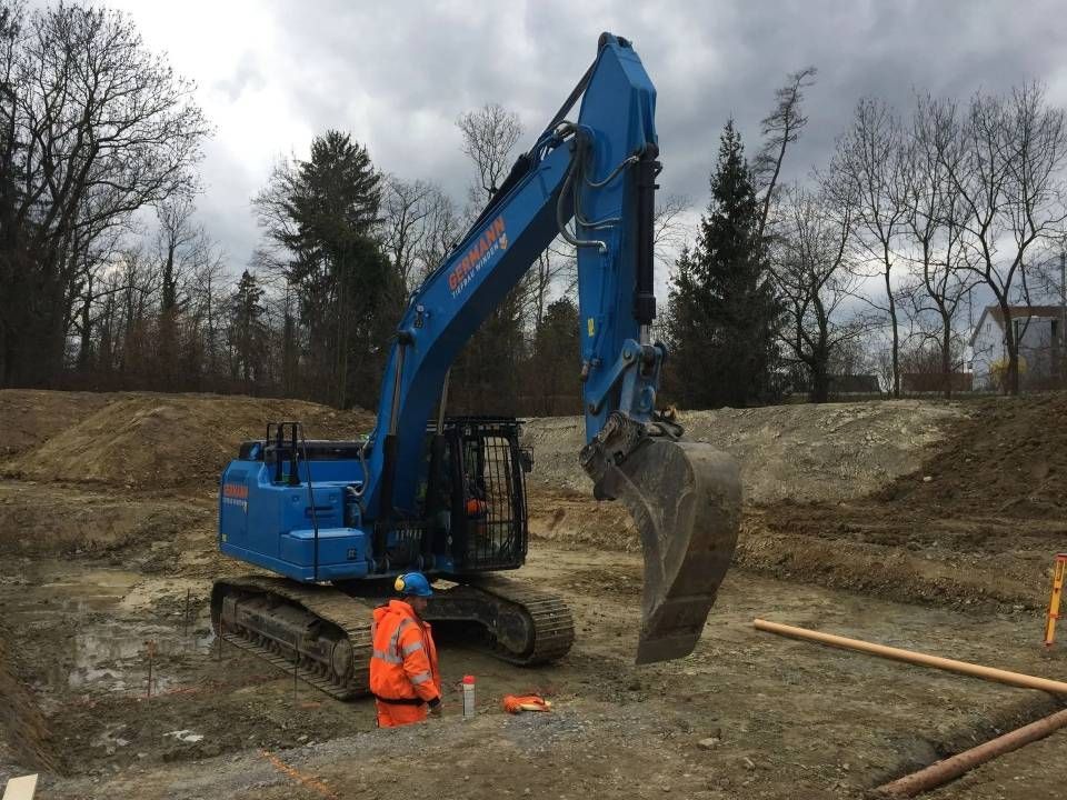 Blauer Bagger auf einer Baustelle, Fahrer in orangefarbener Weste.
