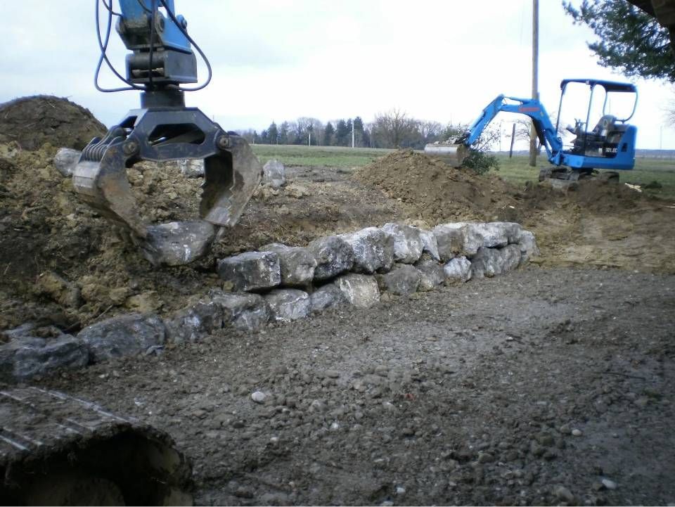 Baustelle mit einem Bagger, der Steine ​​zum Bau einer Stützmauer im Freien platziert.