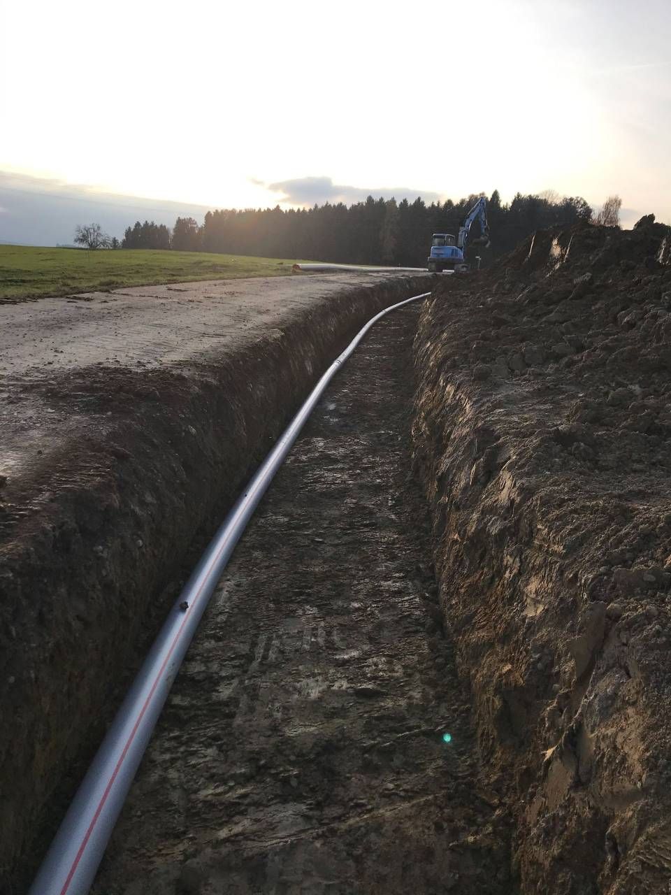 Eine in einem langen Graben auf einer Baustelle verlegte Pipeline, im Hintergrund Erdhügel und Baumaschinen.