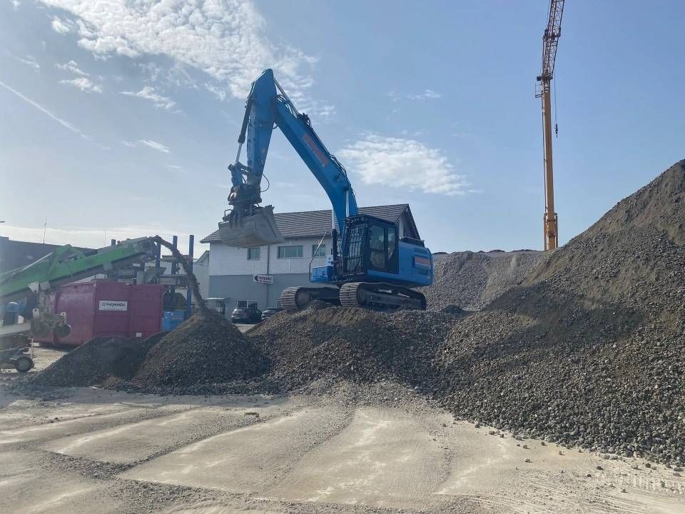 Ein blauer Bagger transportiert Kies auf einer Baustelle.