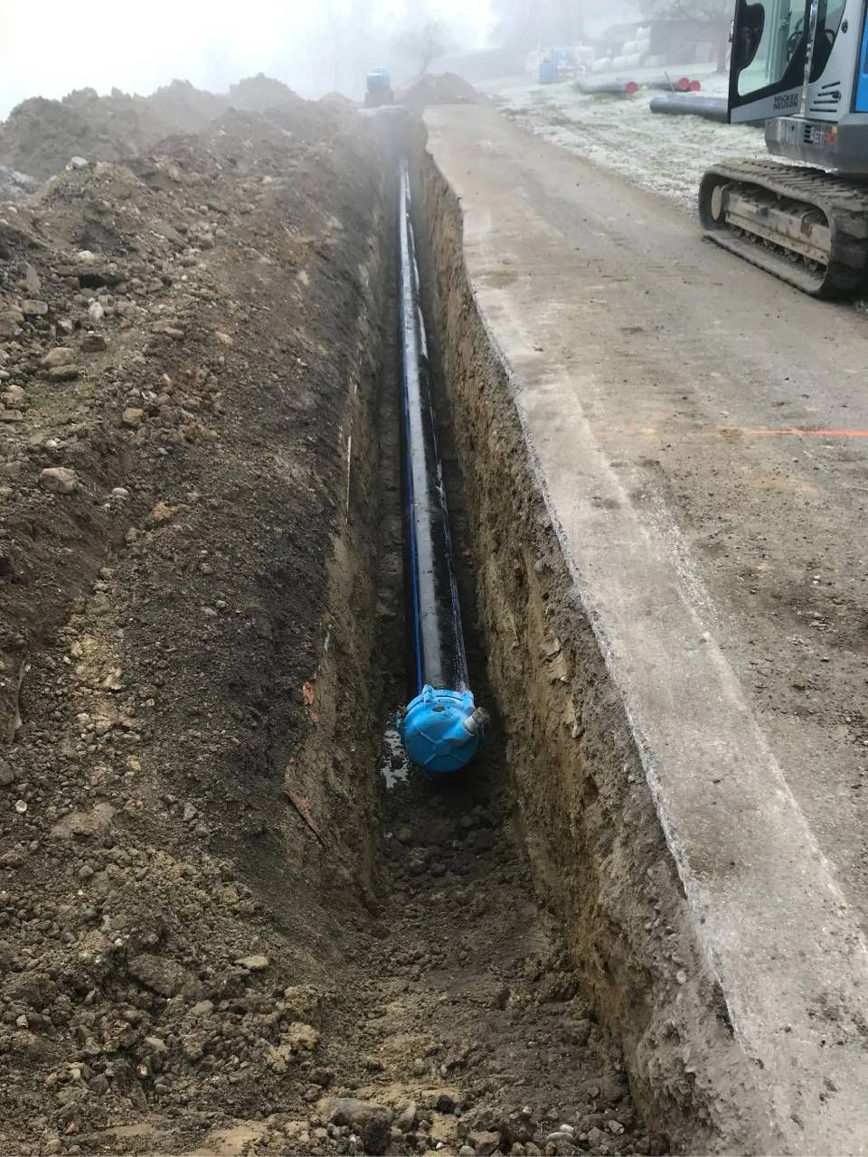 Entlang einer Strasse wurde ein Graben ausgehoben, in den ein schwarzes Rohr verlegt wurde; Baustelle.