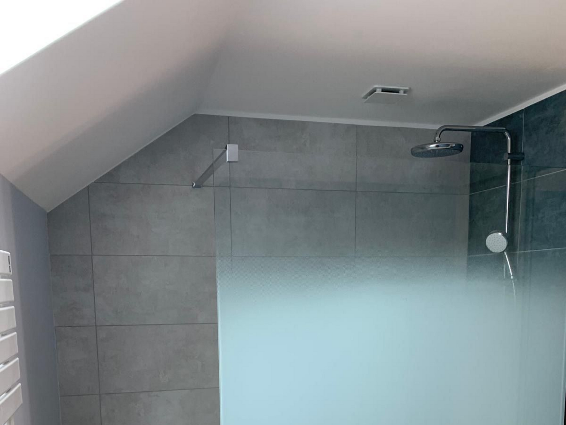 Salle de bains carrelée de gris avec plafond mansardé et douche à l'italienne.
