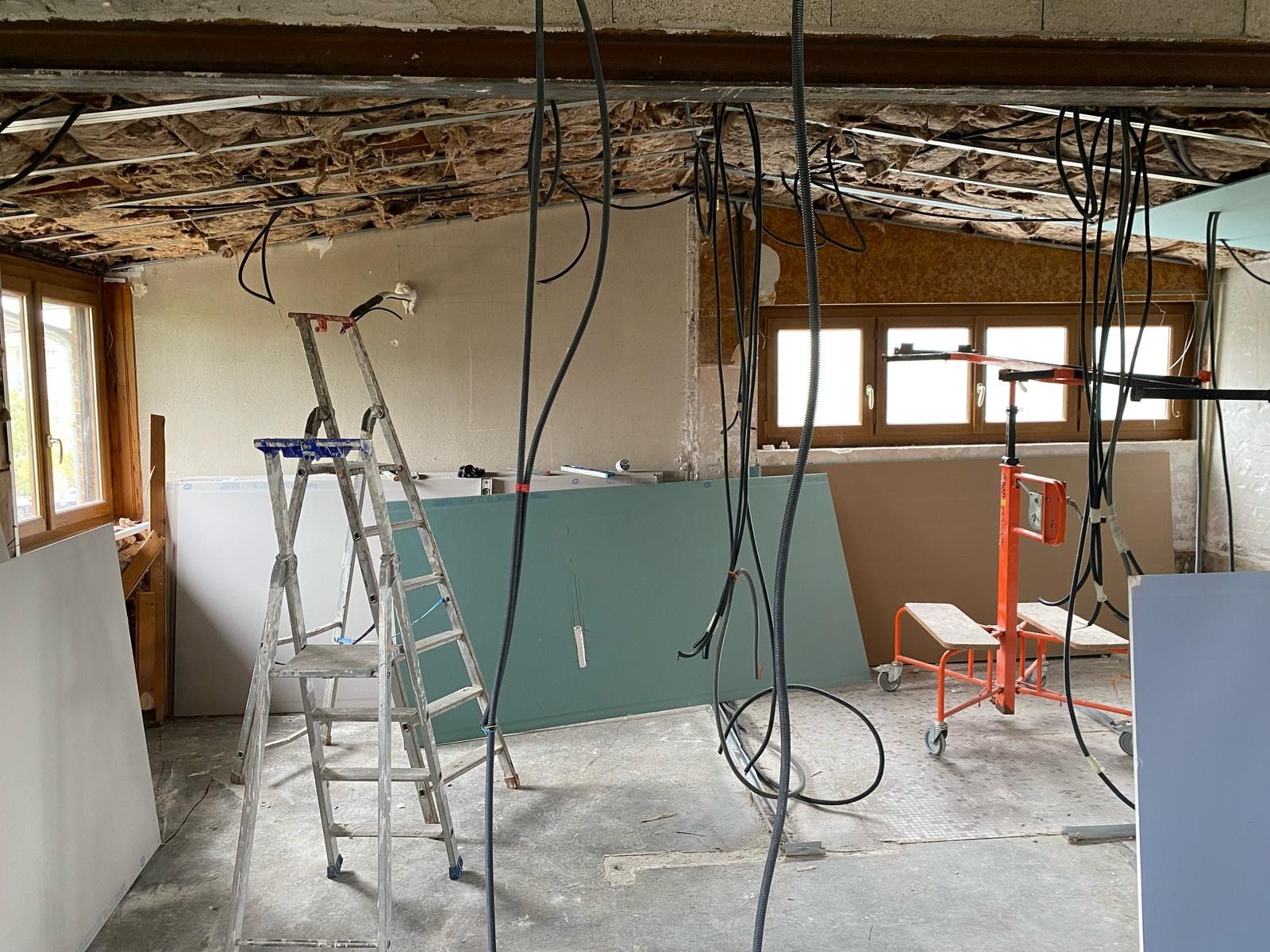 Chantier de rénovation avec matériels, câbles électriques apparents et murs et plafonds intérieurs non finis.