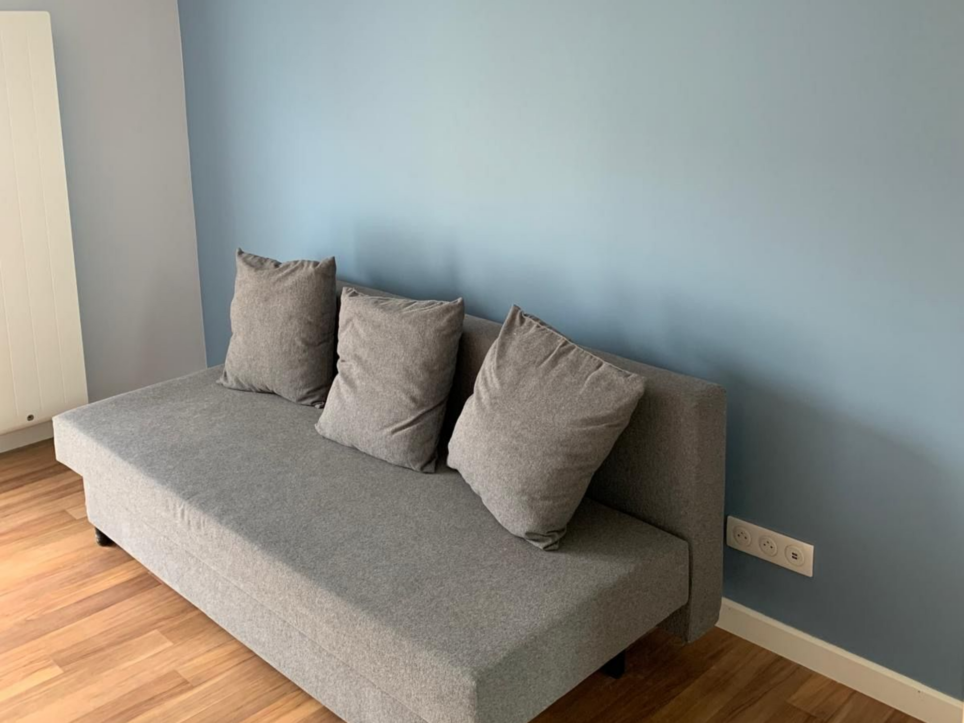 Canapé gris avec trois coussins contre un mur bleu dans une pièce minimaliste.