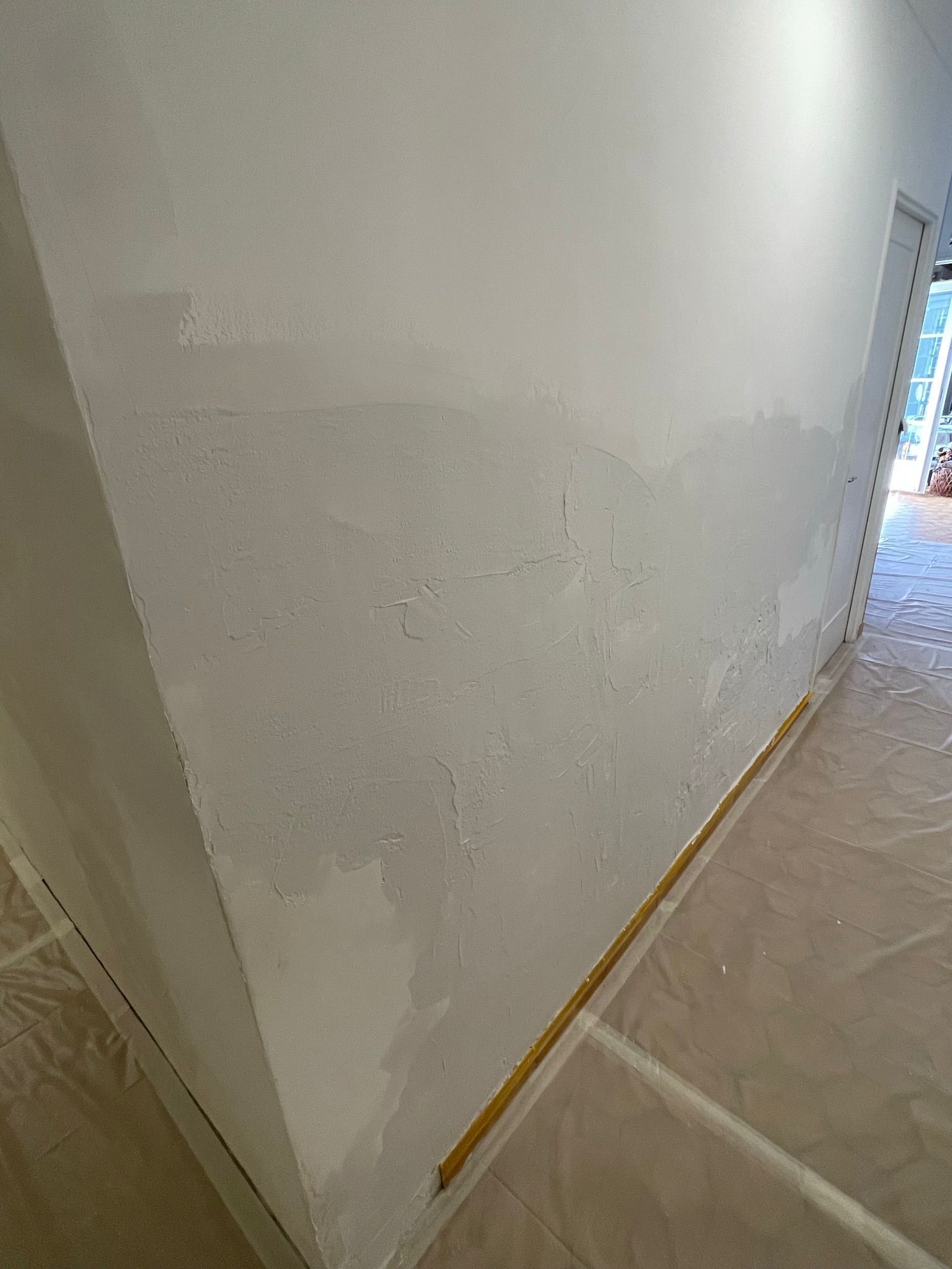 Couloir étroit avec un mur blanc rénové, un sol recouvert d'une bâche pour le protéger.