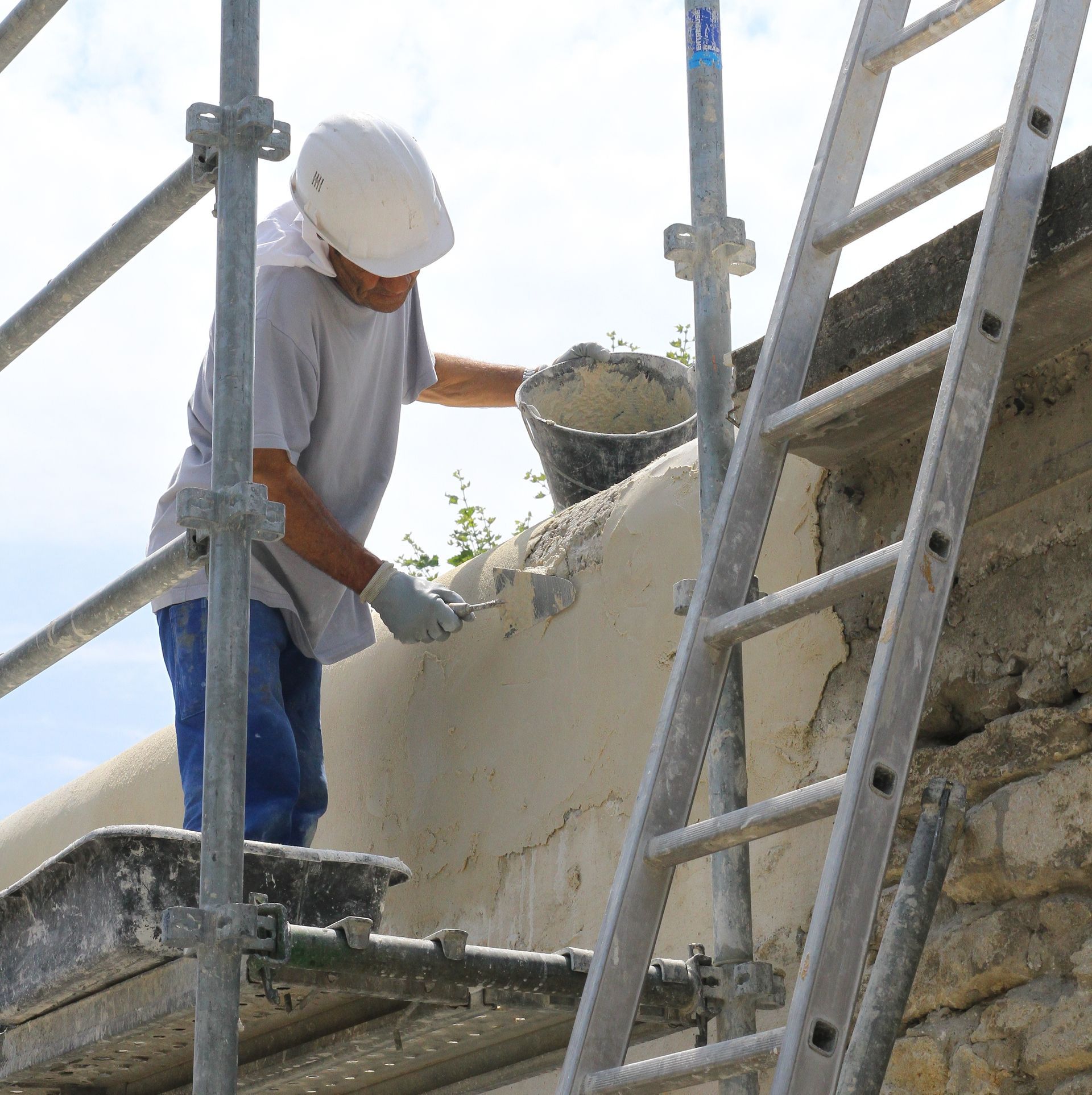 Un ouvrier du bâtiment applique un enduit sur un mur à côté d'une échelle et d'un échafaudage.