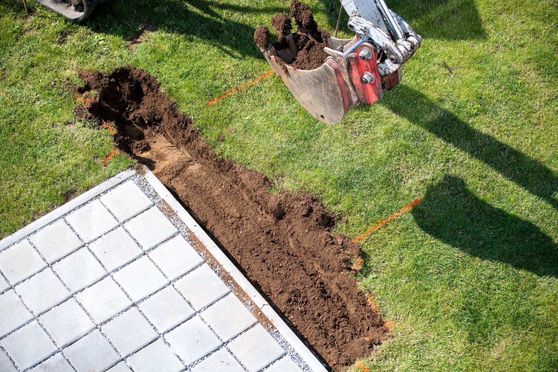 Un engin de chantier creuse une tranchée dans un jardin.