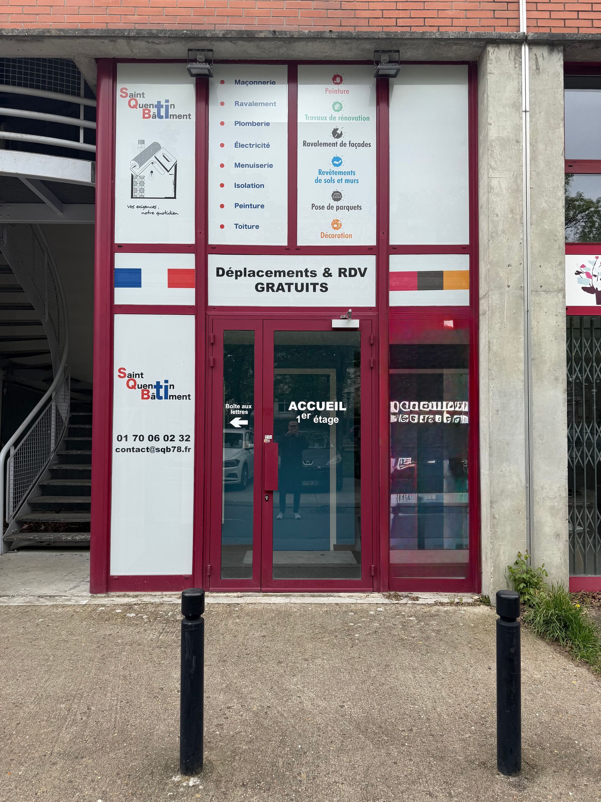 Façade vitrée avec encadrements et enseignes rouges, vue de l'extérieur depuis une allée piétonne en béton.