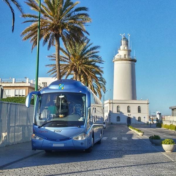 Un autobús azul está estacionado frente a un faro.