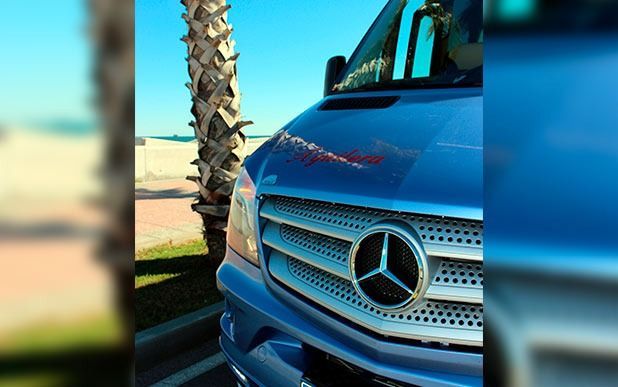 Una camioneta Mercedes azul está estacionada en un estacionamiento al lado de una palmera.