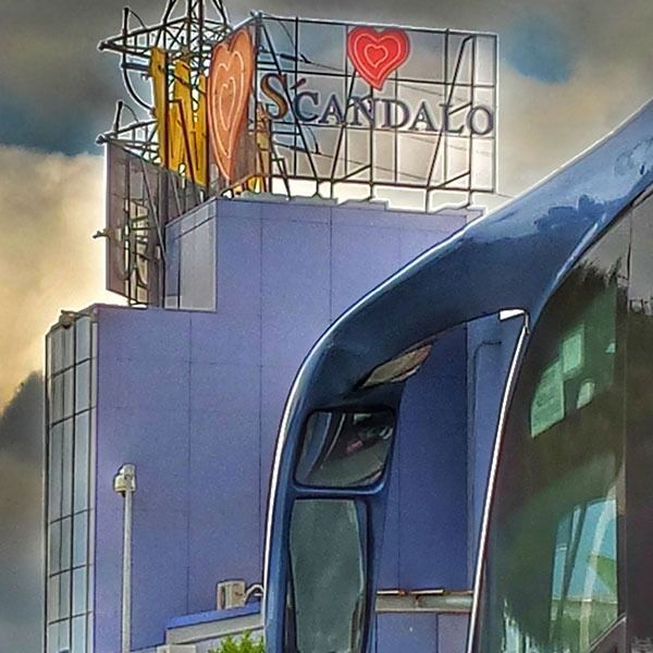 Un autobús azul está estacionado frente a un edificio que dice scandalo