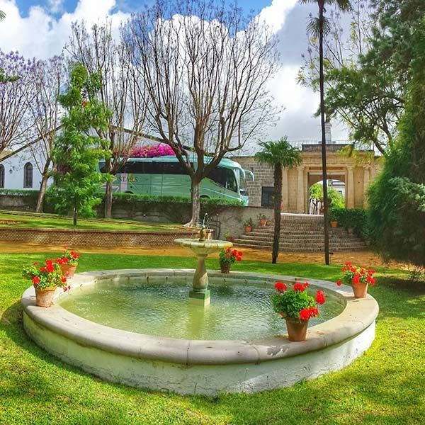 Una fuente en un parque con un autobús al fondo.
