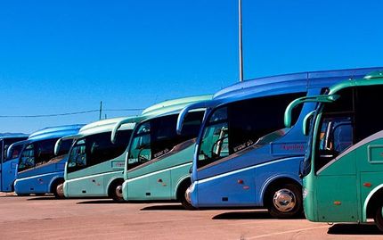 Una fila de autobuses azules y verdes están estacionados en un estacionamiento.