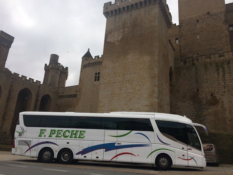 Un autobús blanco con la palabra F. Peche en el costado está estacionado frente a un castillo.