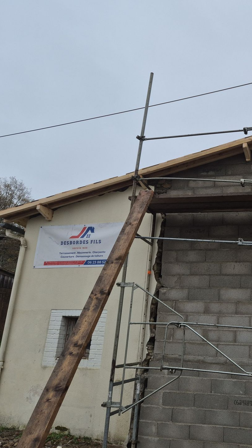 Chantier : échafaudage à côté d'un bâtiment en parpaings dont le toit est partiellement construit.