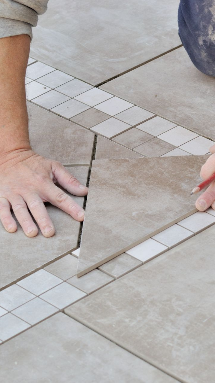 Poseur de carrelage, traçant au crayon une marque pour la découpe. Frise décorative en diagonale entre les carreaux plus grands.