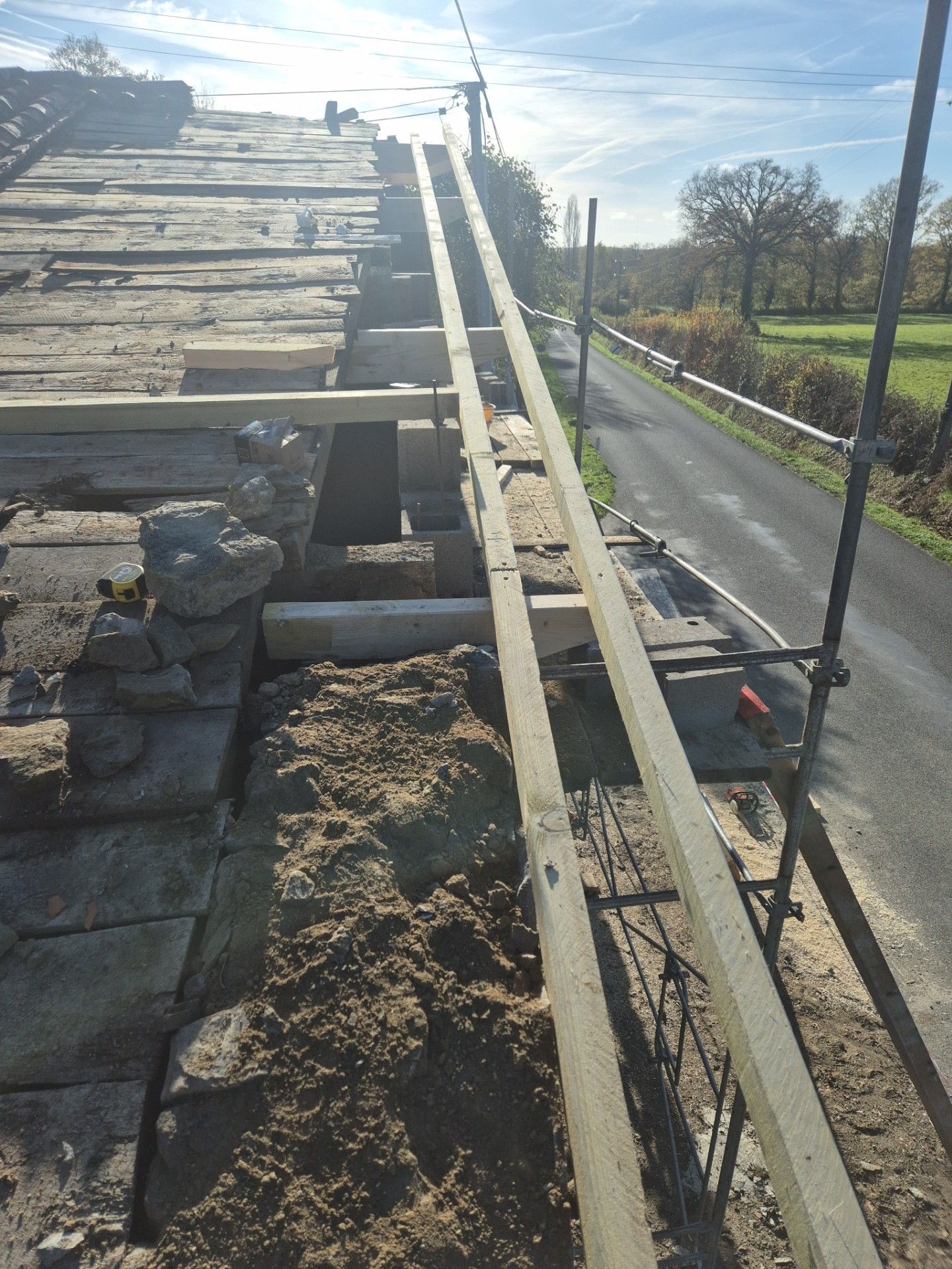 Toit avec échafaudage, échelle et sable, donnant sur une route et un champ par une journée ensoleillée.