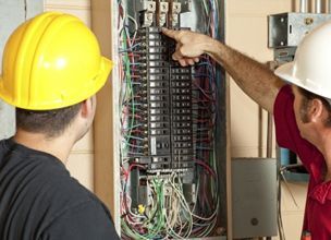 Dos hombres que llevan cascos están trabajando en un panel eléctrico.