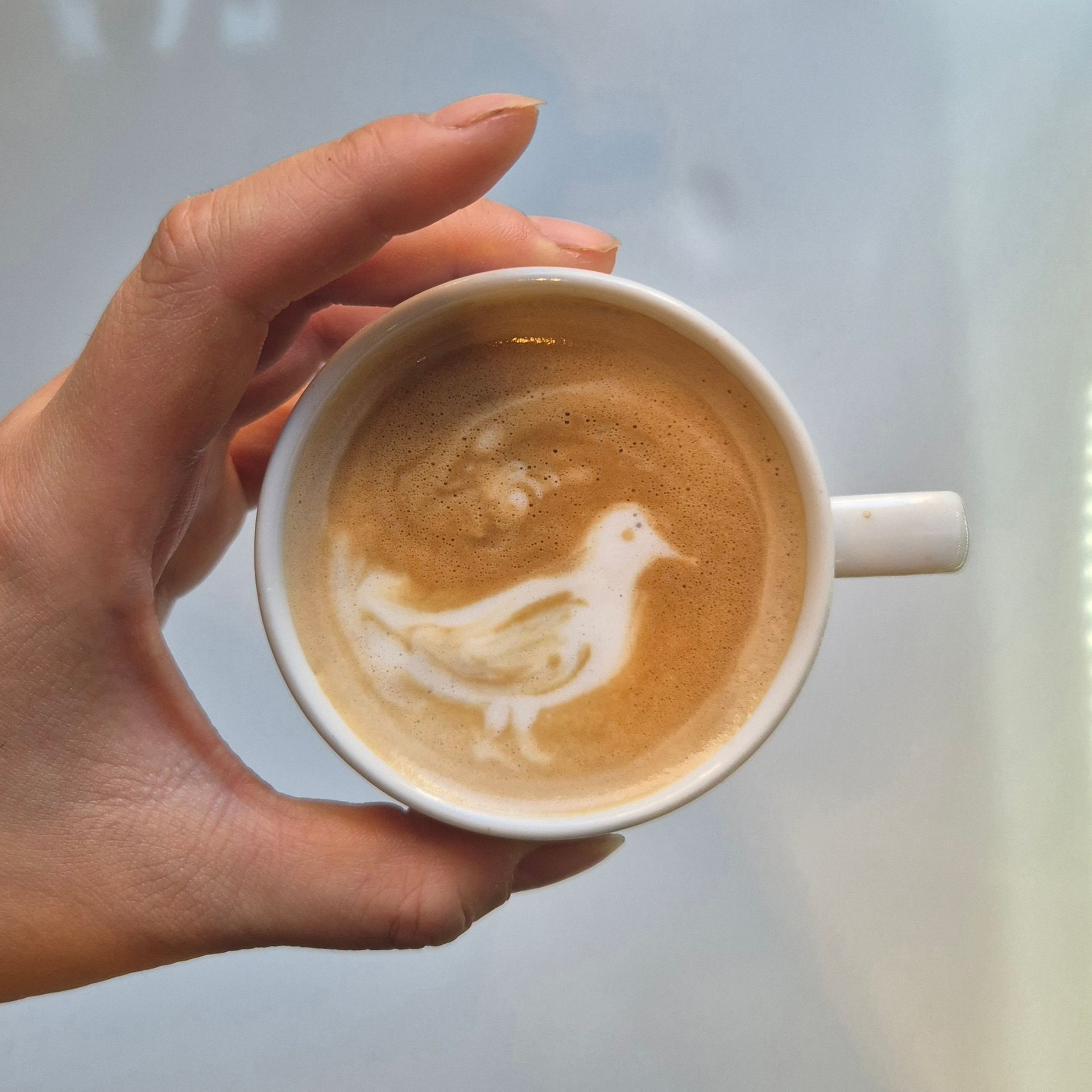 Mano sosteniendo una taza de café con arte latte sobre un fondo liso.