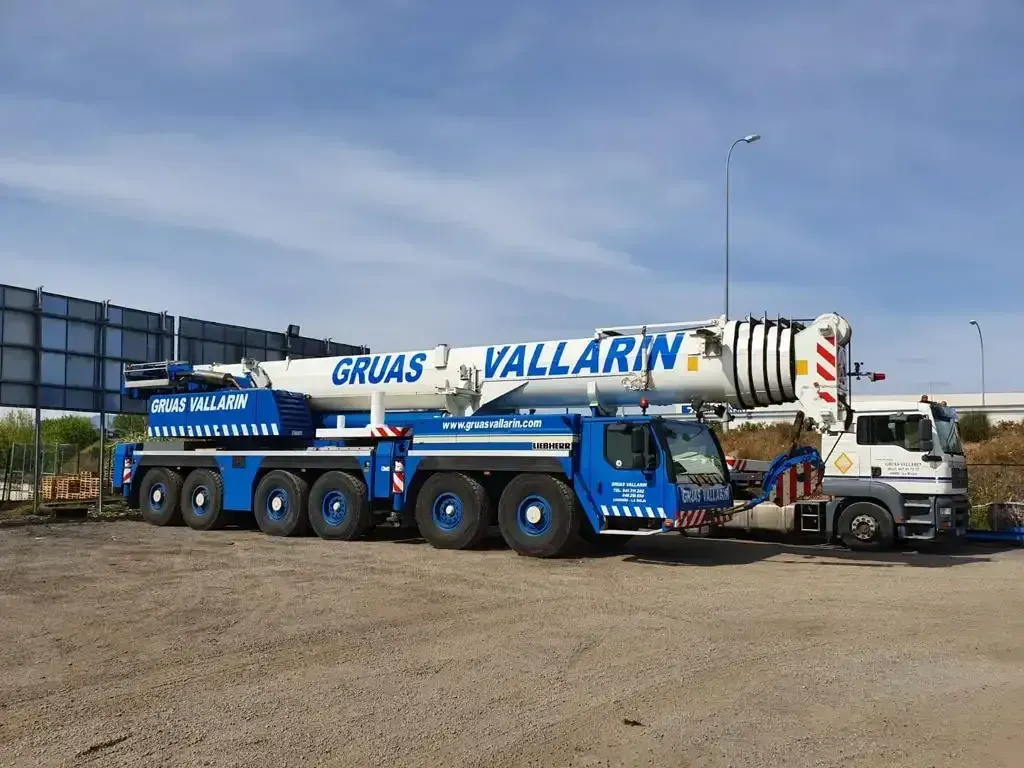 Una gran grúa está estacionada en un estacionamiento al lado de un camión.