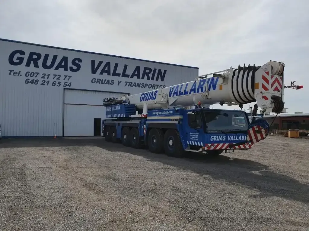 Una grúa grande está estacionada frente a un edificio que dice gruas vallarin