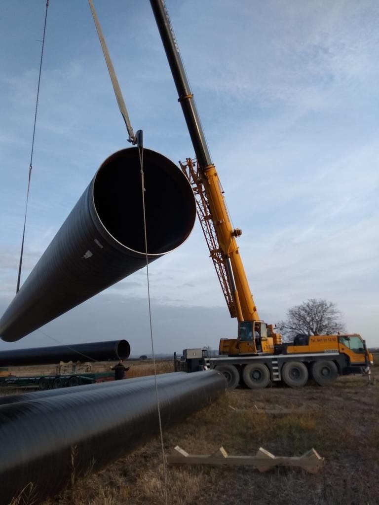 Una grúa levanta una tubería grande en un campo.