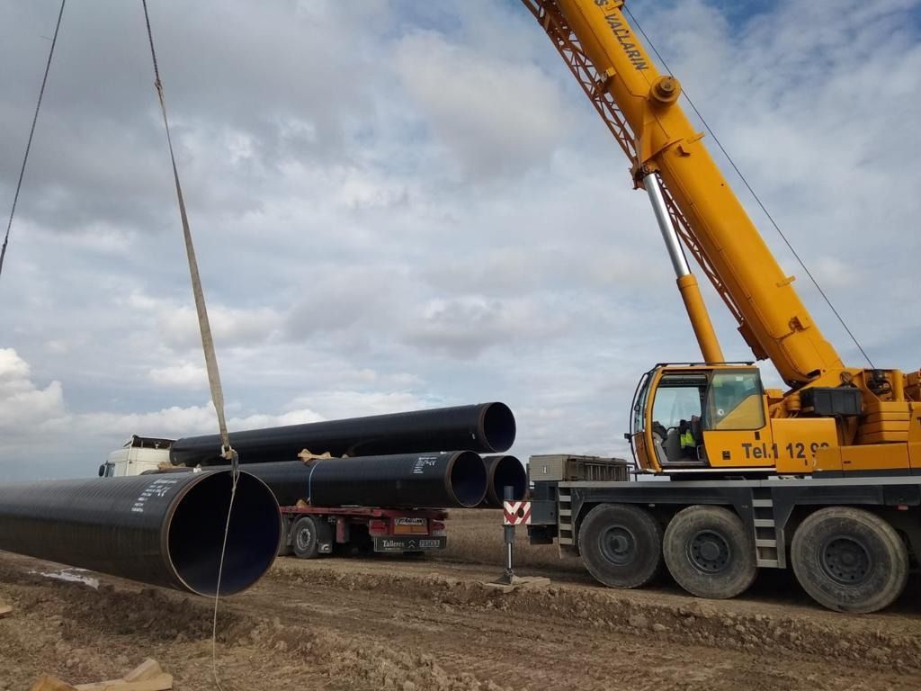 Una grúa amarilla está levantando una pila de tuberías