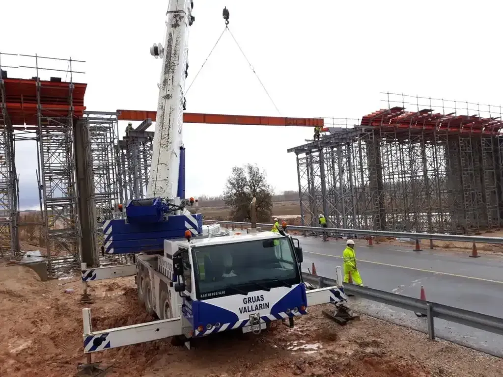 Una grúa está levantando un puente sobre una carretera.