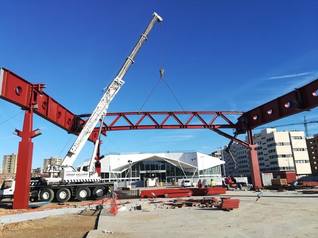 Una grúa grande está levantando una estructura metálica en un sitio de construcción.