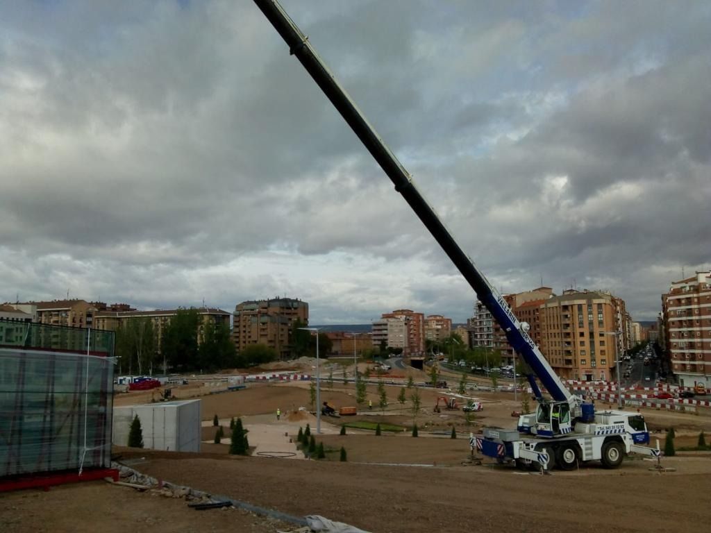 Una gran grúa está sentada en un campo con edificios al fondo.