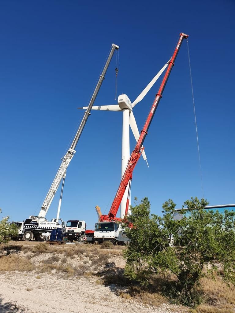 Dos grúas están trabajando en una turbina eólica en un campo