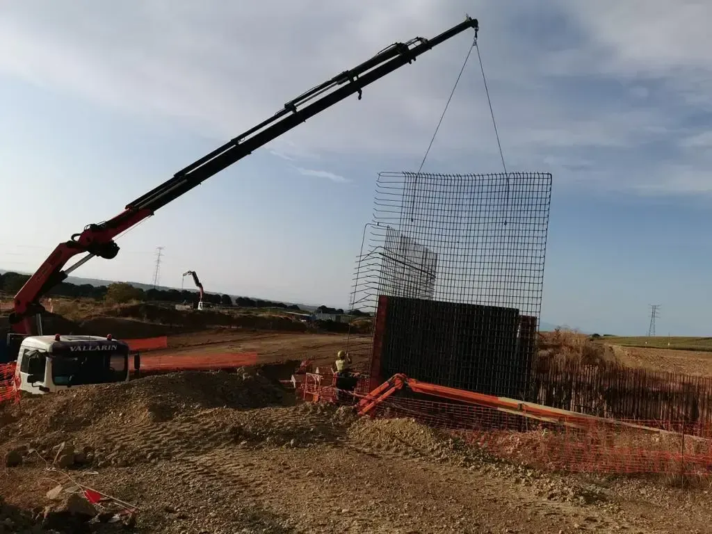 Una grúa está levantando una gran pieza de metal en un campo de tierra.